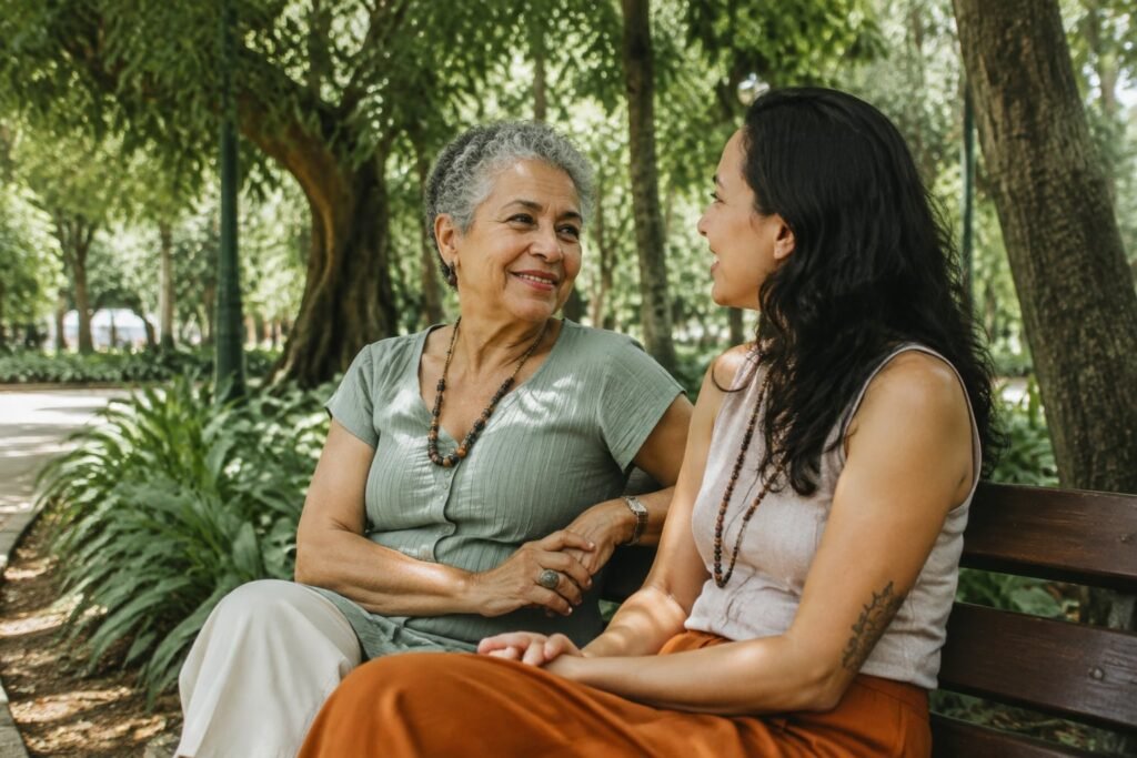 Mulher idosa e amiga mais jovem conversam sentadas em um banco de jardim.